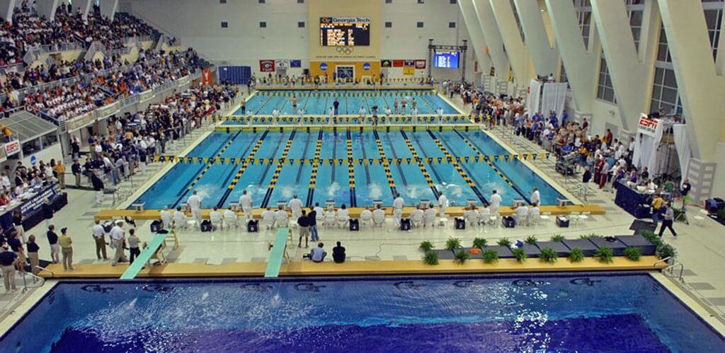 Stadio di nuoto pieno di spettatori durante una competizione universitaria.